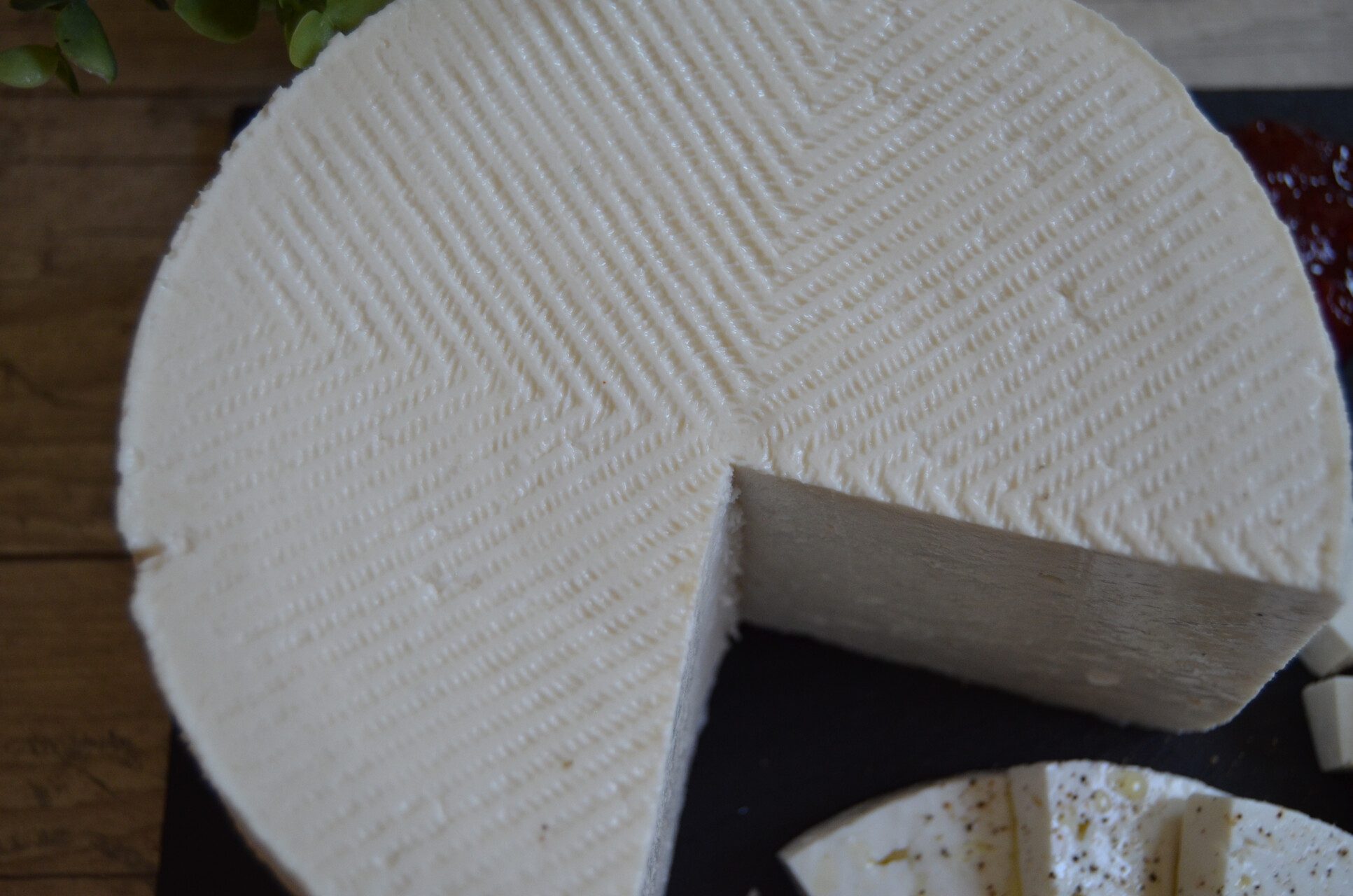 Rueda de queso fresco con el dibujo de espiga que le deja el molde y una cuña cortada, sobre pizarra